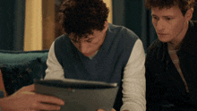 two men are looking at a tablet together and one has curly hair
