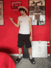 a man wearing a straw hat and black shorts is standing in front of a red wall with posters on it .