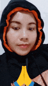 a woman wearing a black and orange hoodie holds her hands together in front of her face