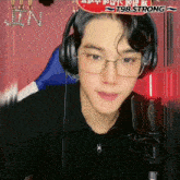 a young man wearing glasses and headphones is sitting in front of a microphone and a sign that says t98 strong