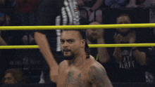 a wrestler in a ring with a referee behind him and a crowd watching