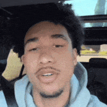 a man with a beard and a gray hoodie is sitting in a car