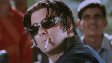 a man wearing sunglasses is smoking a cigarette and looking at the camera .