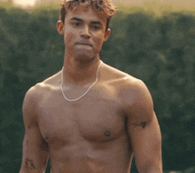 a shirtless man with a necklace around his neck has a tattoo on his chest that says ' x ' on it