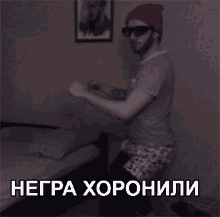 a man wearing sunglasses and a hat is dancing in front of a bed with the word negra written in white letters
