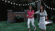two women dancing in a backyard with a string of lights