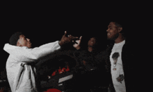 three men are standing in front of a car and one of them is wearing a hoodie that says ' supreme ' on it