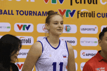 a woman wearing a number 11 jersey stands in front of a yellow banner