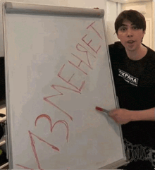 a man is standing in front of a whiteboard with russian writing on it and pointing at it .
