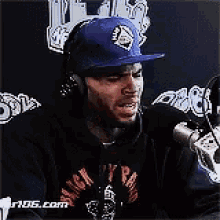 a man wearing headphones and a hat is talking into a microphone .