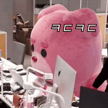 a pink stuffed animal is sitting at a desk with a mac computer in front of it