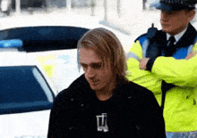 a man in a black shirt is standing in front of a police car while a police officer looks on .