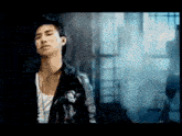 a young man in a leather jacket is standing in front of a window .