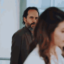 a man with a beard is looking at a woman in a white shirt .