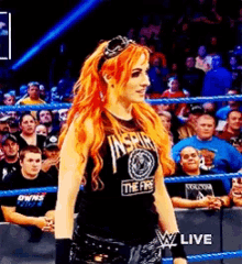 a woman with red hair is standing in a wrestling ring wearing a black shirt that says the fire .