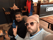 two men are posing for a picture in front of a kitchen sign