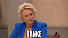 a woman in a blue jacket is sitting in front of a microphone with the word danke written on her face .