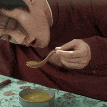 a man in a red shirt is eating soup from a bowl with a spoon