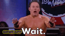 a wrestler is standing in a ring with his mouth open and the words wait written on the screen behind him .
