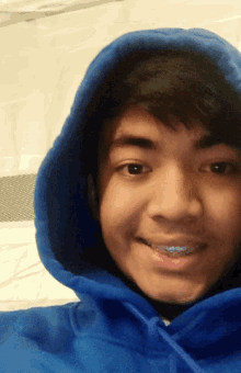 a young man wearing a blue hoodie with braces on his teeth smiles for the camera