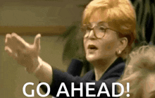 a woman with glasses says go ahead with her hands outstretched