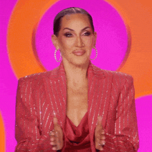 a woman in a red suit and hoop earrings is clapping her hands .