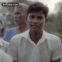a young man in a white shirt is looking at the camera while standing in a crowd of people .