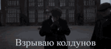 a man in a suit and tie stands in front of a large brick building with a sign in russian