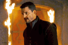 a man with a beard is standing in front of a wall of fire