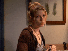 a woman wearing a brown sweater and a necklace looks at the camera