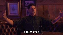 a man sitting at a table with his arms outstretched and the words heyyy on the bottom