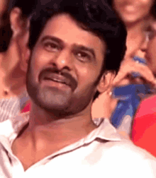 a man with a mustache is sitting in a crowd of people and smiling .