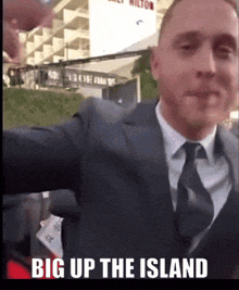 a man in a suit and tie taking a selfie with the words big up the island below him