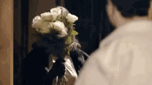 a woman is holding a bouquet of white roses in her hand and looking at a man .