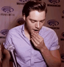 a man in a purple shirt is covering his mouth with his hand while talking into a microphone .