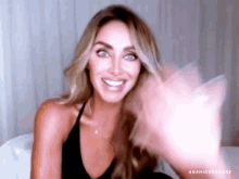 a woman in a black tank top is smiling and waving her hand