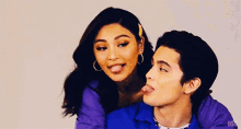 a man and a woman are sticking their tongues out . the woman is wearing a purple jacket .