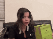 a woman sitting on a couch holding a green box