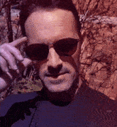 a man wearing sunglasses and a black shirt looks at the camera
