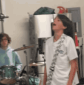 a boy is singing in front of a drum set while another boy plays drums .