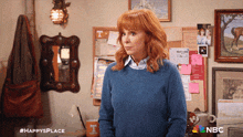 a woman wearing a blue sweater is standing in front of a bulletin board with a t on it
