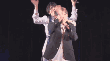 two men singing into microphones on a stage with their hands in the air