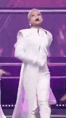a woman in a white suit is dancing on a stage with a purple background .