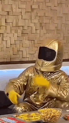 a man in a gold space suit is sitting at a table with a bowl of chips .