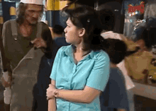 a woman in a blue shirt is standing next to a man in overalls in a crowd .