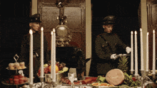 two men in military uniforms standing in front of a table with candles and food