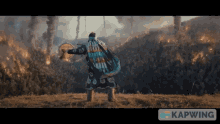 a man is playing a drum in front of a forest fire and the word kapwing is on the bottom