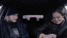 two young men are sitting in a car and one of them is wearing a beanie and the other is wearing a jacket