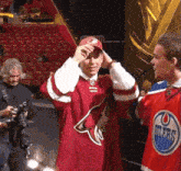 a man wearing a red arizona coyotes jersey talks to a reporter
