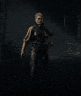 a woman standing in a dark forest with a gun in her belt